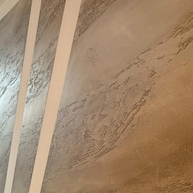 Strukturierte Wand mit abwechselnd glatten und rauen, silbrig glänzenden Streifen in einem Flur.