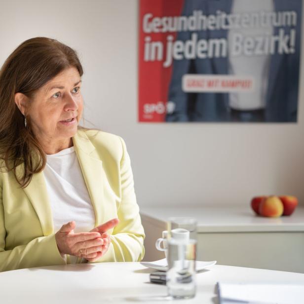 Eine Frau im hellgelben Blazer sitzt an einem Tisch, im Hintergrund ein SPÖ-Plakat.