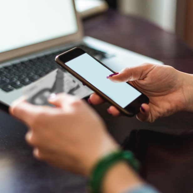 Eine Person nutzt Smartphone und Kreditkarte an einem Laptop für einen Online-Kauf.