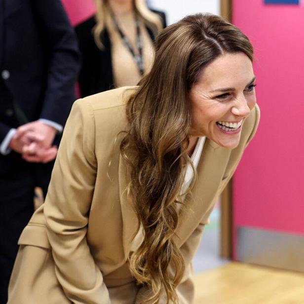 Prinzessin Kate lacht in einem beigen Hosenanzug, leicht nach vorne gebeugt.