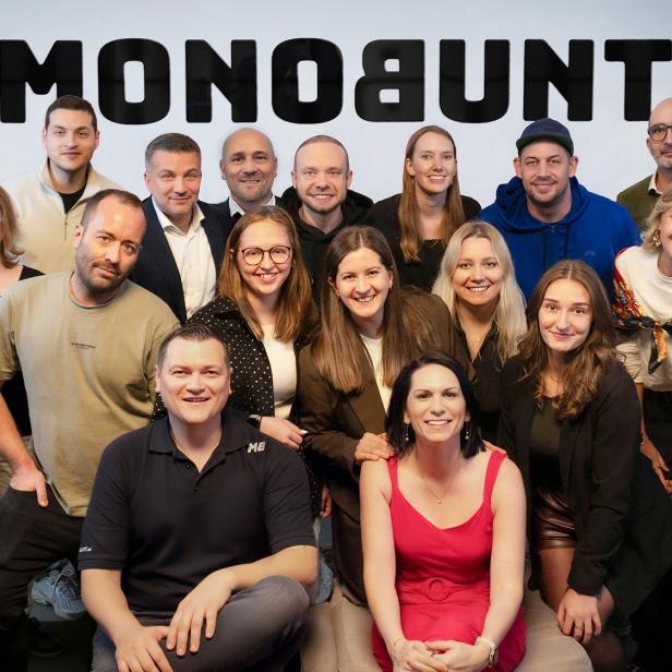 Gruppenfoto von 16 Personen vor einer Wand mit dem Schriftzug „MONOBUNT“.