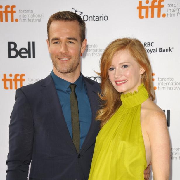 James Van Der Beek im Anzug und seine Ehefrau Kimberly Van Der Beek im grünen Kleid stehen lächelnd nebeneinander vor einer Sponsorenwand. Aufgenommen wurde das Foto im Jahr 2013.