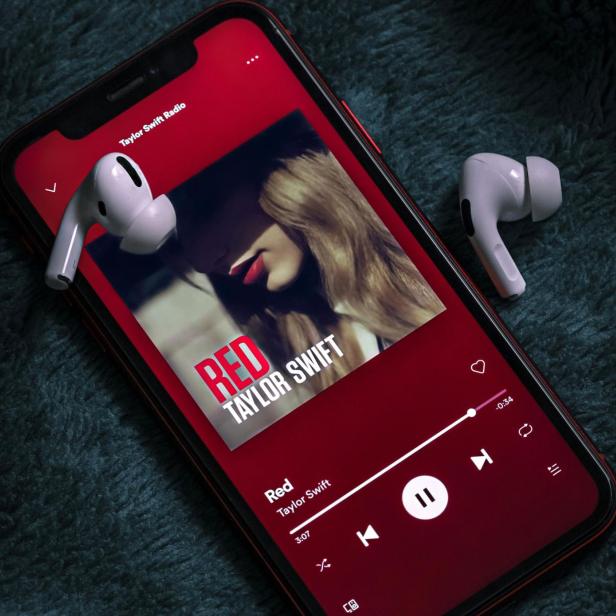 Smartphone mit Spotify-App zeigt das Album "Red" von Taylor Swift und zwei kabellose Kopfhörer.