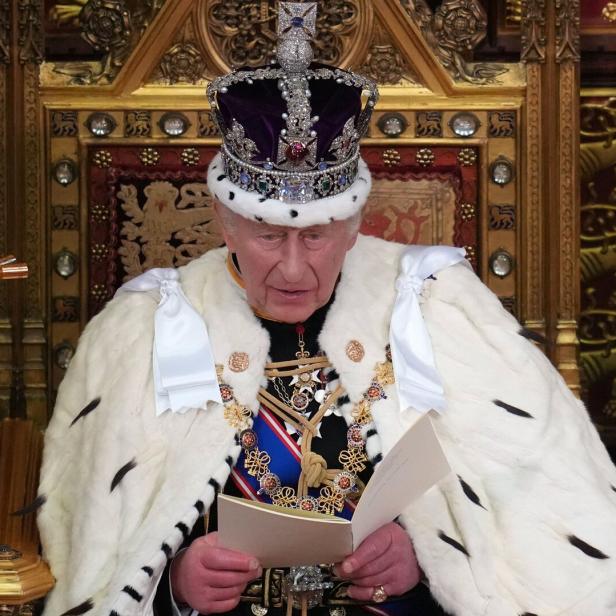 König Charles III. mit Krone und Hermelinmantel liest von einem Blatt Papier auf einem goldenen Thron.
