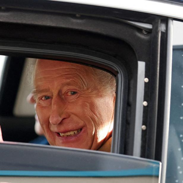 König Charles III. lächelt aus einem Autofenster und winkt.
