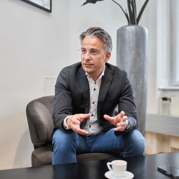 Ein Mann mit Brille, Sakko und Jeans sitzt gestikulierend in einem Sessel.