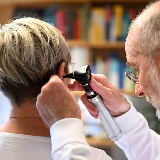 Ein Arzt untersucht mit einem Otoskop das Ohr einer Person mit kurzem, blondem Haar.