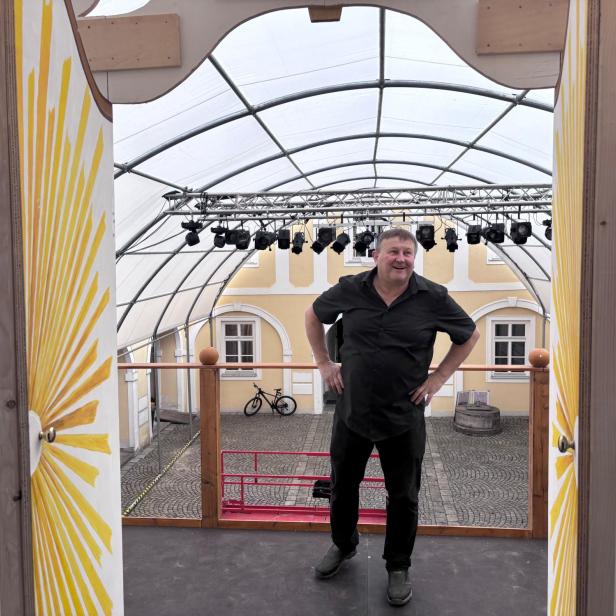 Ein Mann steht auf einer überdachten Theaterbühne mit gelbem Bühnenbild und Blick nach draußen.