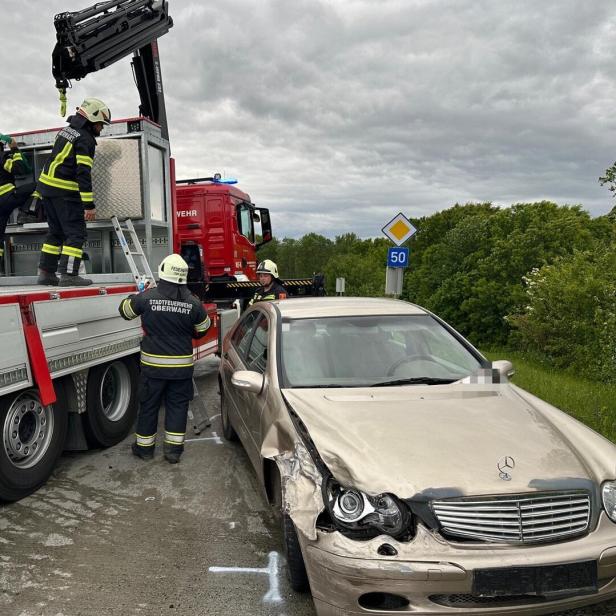 Mehrere Feuerwehrleute sichern ein beschädigtes Auto neben einem Einsatzfahrzeug auf einer Landstraße.