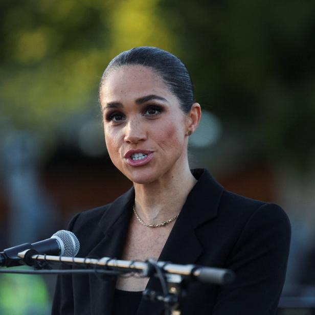 Meghan, Herzogin von Sussex, spricht in einem schwarzen Blazer vor einem Mikrofon.