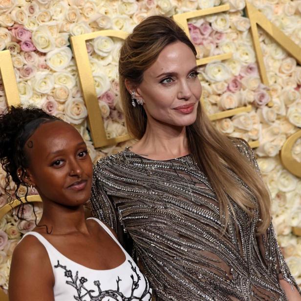 Angelina Jolie posiert mit Tochter Zahara vor einem Rosenhintergrund.