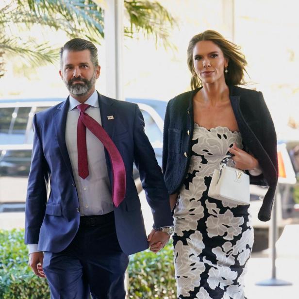 Donald Trump Jr im Anzug und Bettina Anderson im Blumenkleid gehen Händchen haltend spazieren.