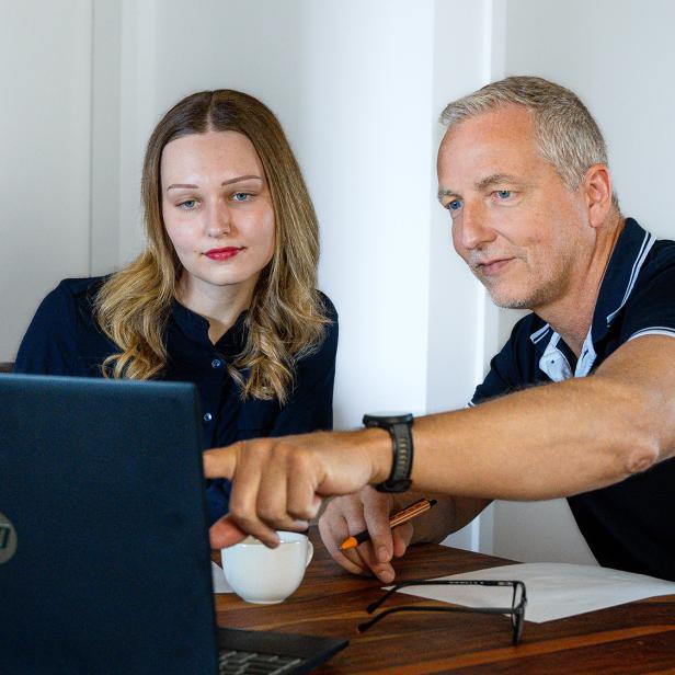 Zwei Personen besprechen gemeinsam Inhalte auf einem Laptop an einem Holztisch.