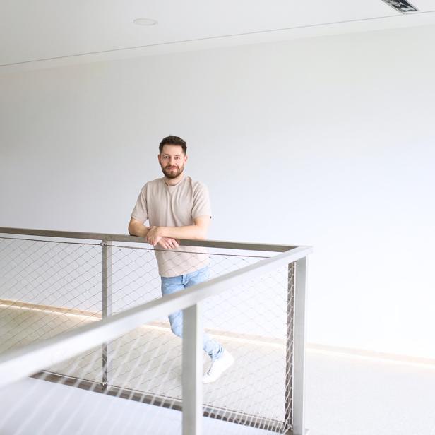 Ein Mann lehnt an einem modernen Geländer in einem hellen, minimalistischen Innenraum.