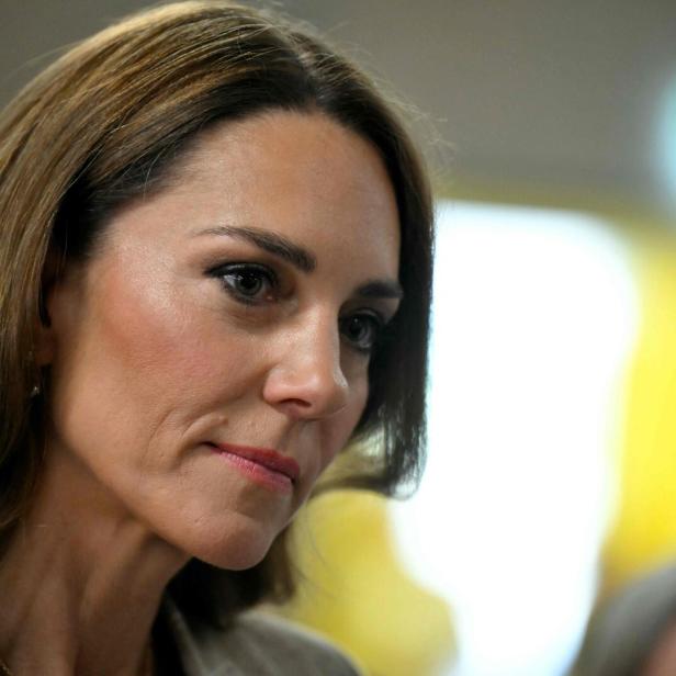 Prinzessin Kate mit langen braunen Haaren blickt nachdenklich zur Seite, im Hintergrund unscharfe Lichter.