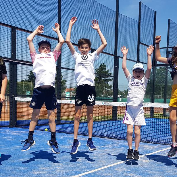 Fünf Kinder springen lachend auf einem Sportplatz in die Luft.