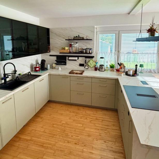 Eine moderne, helle Küche mit großer Arbeitsfläche, schwarzen Akzenten und Fenstern mit Blick ins Grüne.