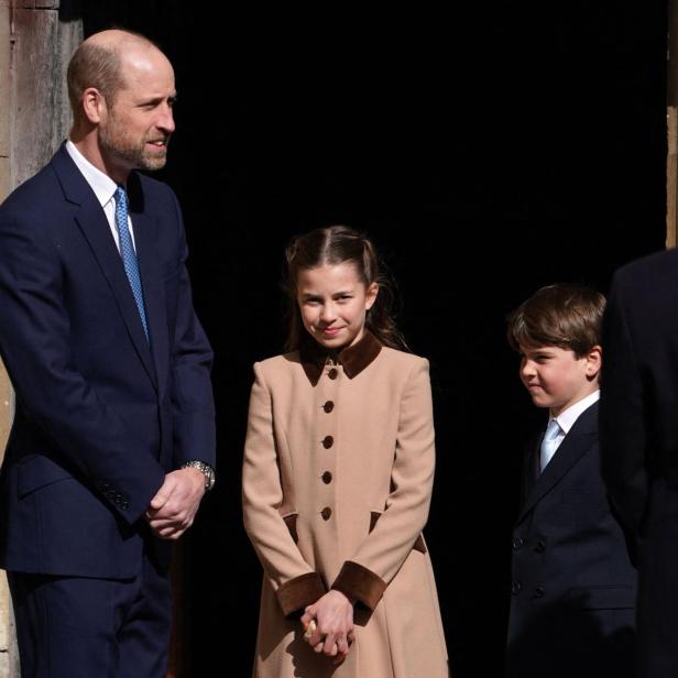 Prinz William steht mit Prinzessin Charlotte und Prinz George vor einem Gebäude.