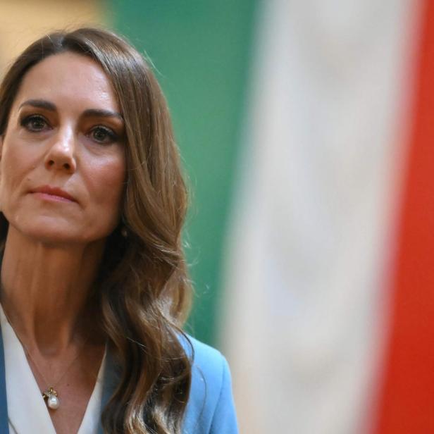 Prinzessin Kate mit braunen, gewellten Haaren und blauem Blazer schaut zur Seite.