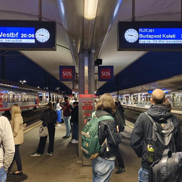 Bahnsteig in Linz mit Anzeigen und wartenden Fahrgästen.
