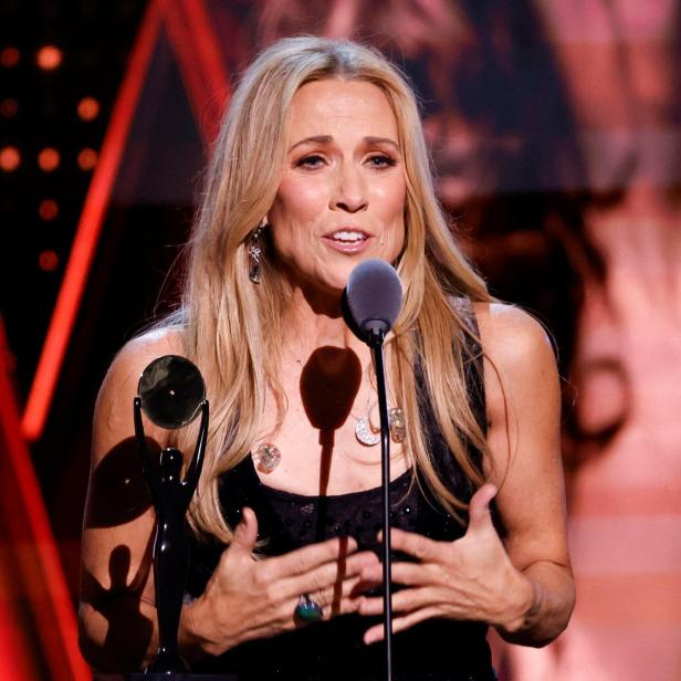 Sheryl Crow spricht mit einer Auszeichnung in der Hand vor einem Mikrofon.