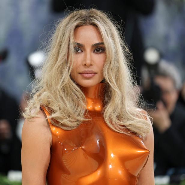 Kim Kardashian trägt ein orangefarbenes Kleid und blondes, gewelltes Haar.