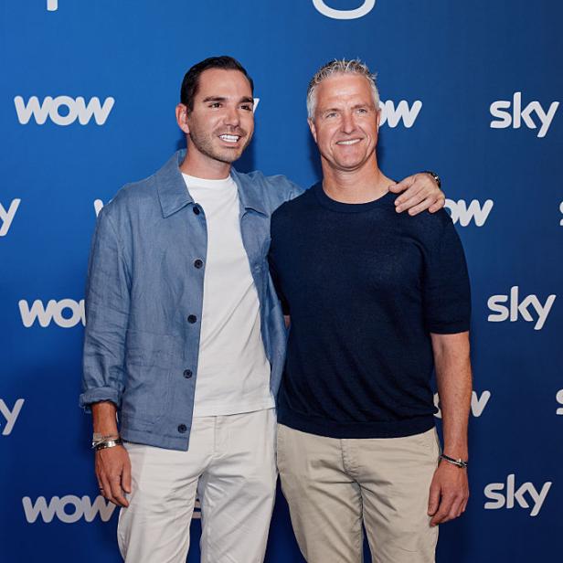 Étienne Bousquet-Cassagne und Ralf Schumacher posieren gemeinsam lächelnd vor einer blauen Wand mit den Logos von Sky und Wow.