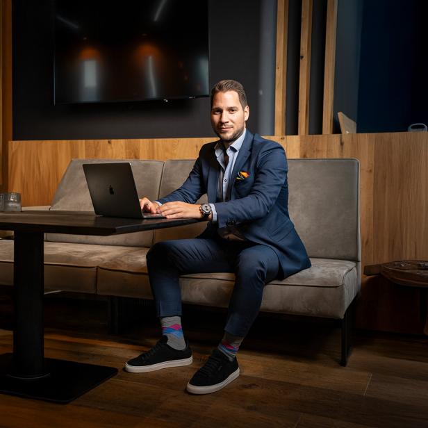 Ein Mann im Anzug sitzt mit Laptop an einem Tisch in modernem, holzvertäfeltem Raum.