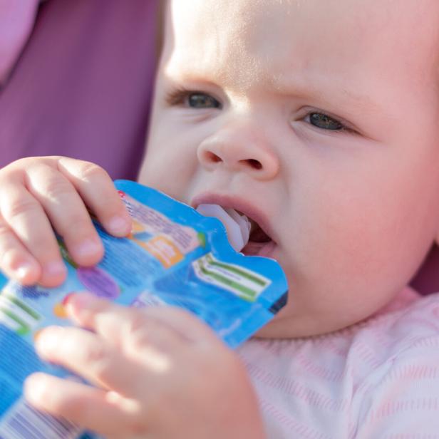 Ein Baby hält einen blauen Quetschbeutel und trinkt daraus.