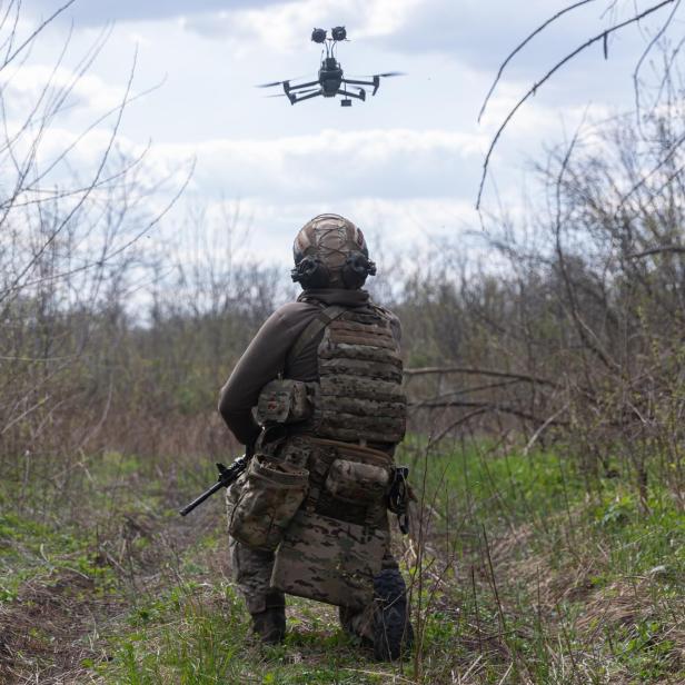 Ein Soldat kniet im Feld und blickt zu einer Drohne in der Luft.