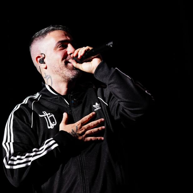 Bushido mit Tätowierungen singt mit Mikrofon in einer schwarzen Adidas-Jacke.