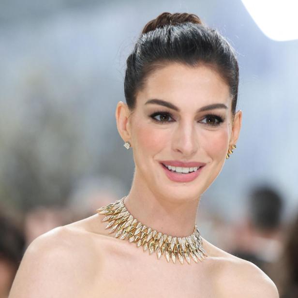 Anne Hathaway. mit hochgesteckten Haaren trägt ein schulterfreies Kleid mit schwarz-weißem Muster und eine auffällige goldene Halskette.