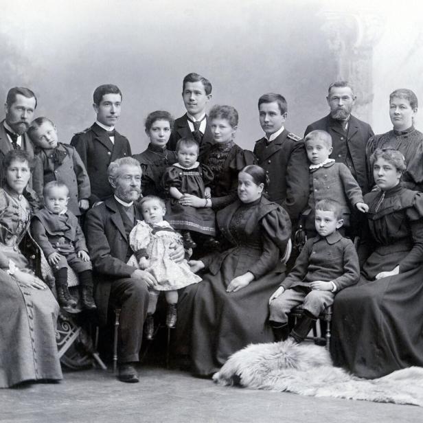 Eine große Familie posiert in altmodischer Kleidung für ein Schwarzweiß-Gruppenporträt.