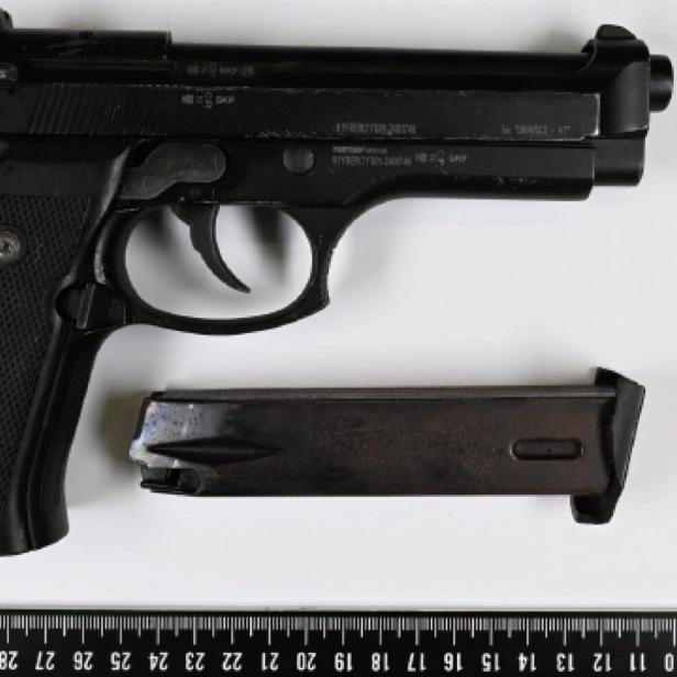 Schwarze Pistole mit separatem Magazin liegt neben einem Lineal auf weißem Untergrund.