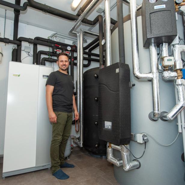Ein Mann steht in einem Technikraum neben einer modernen Heizungsanlage mit vielen Rohren und Speichern.