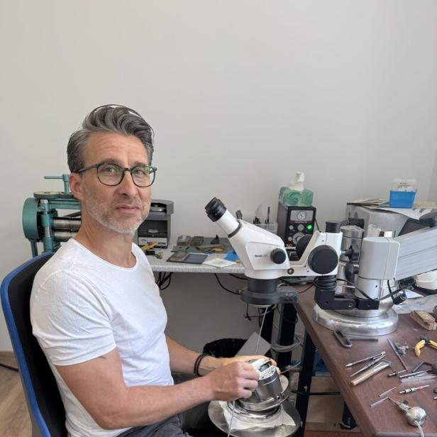Armin Bundschuh sitzt an einem Arbeitstisch mit Mikroskop und Werkzeugen und arbeitet konzentriert an einem kleinen Objekt.