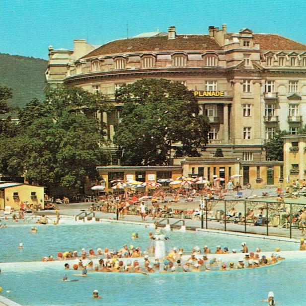 Viele Menschen baden in einem großen Freibad, im Hintergrund stehen Bäume und ein historisches Gebäude mit dem Schriftzug „PLANADE“.
