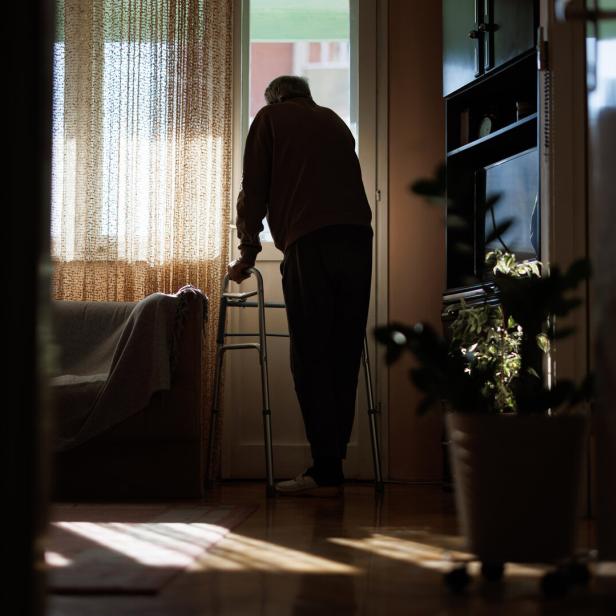 Elderly man with walker looking out window, contemplating life in quiet solitude