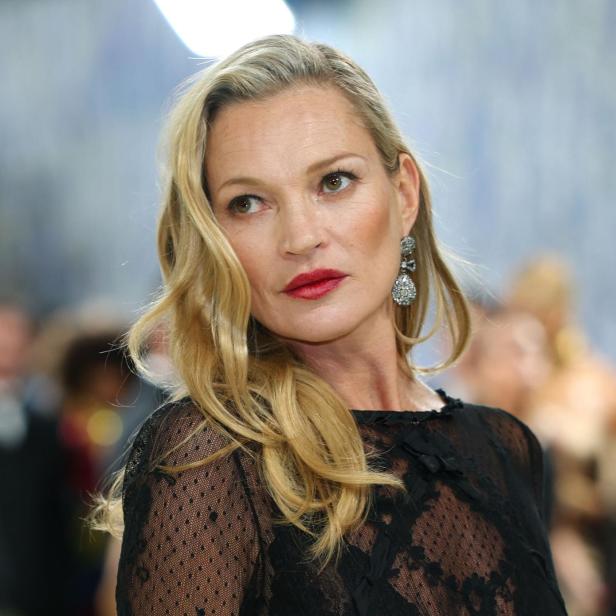 Kate Moss trägt ein transparentes, schwarzes Kleid und auffällige Ohrringe.