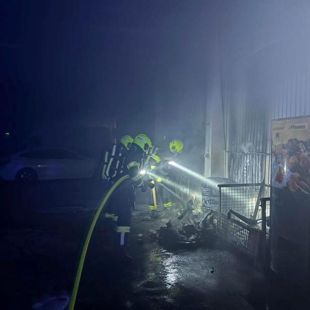 Zwei Feuerwehrleute mit Atemschutz löschen einen Brand in einer verrauchten Halle neben einem Getränkeautomaten.