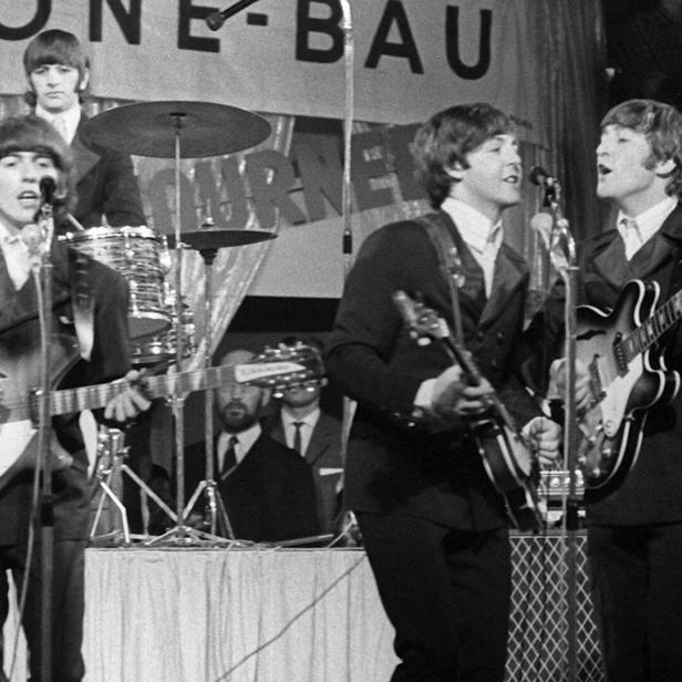 Die Beatles spielen auf einer Bühne vor Mikrofonen und Schlagzeug.