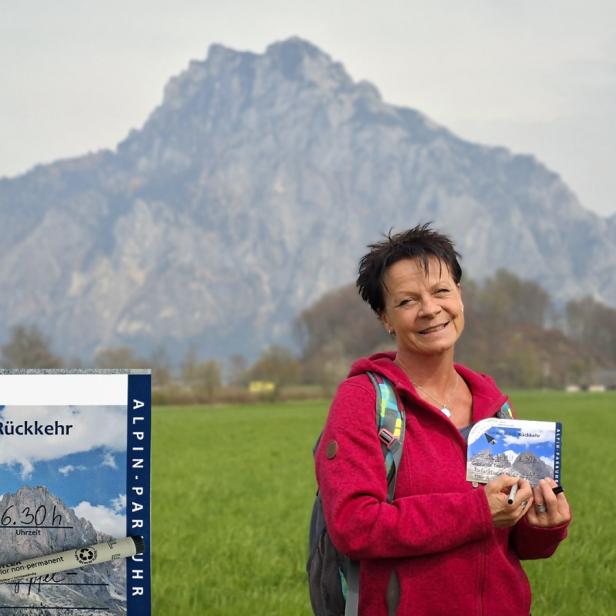 Frau mit ALPINE Parkuhr von KUNSTVOLLER vor Berglandschaft auf einer Wiese.