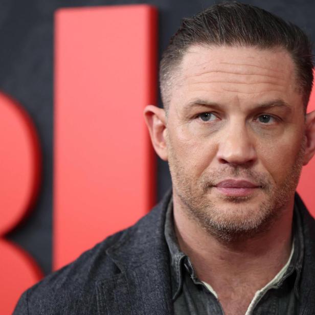 Tom Hardy blickt vor einem roten Hintergrund zur Seite.