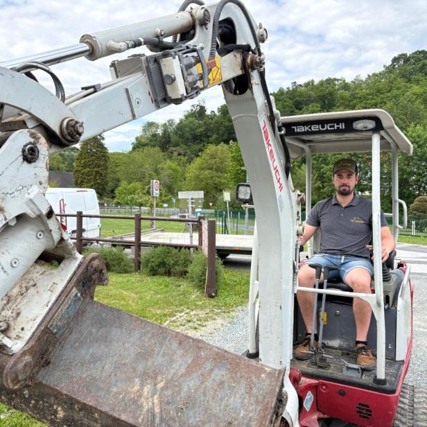 Ein Mann sitzt in einem kleinen Takeuchi-Bagger vor einer grünen Landschaft.
