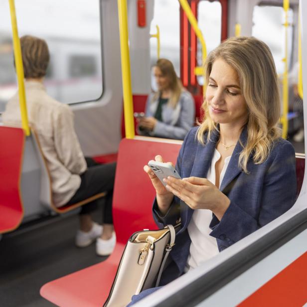 Frau in Businesskleidung sitzt in einer U-Bahn und nutzt ihr Smartphone.