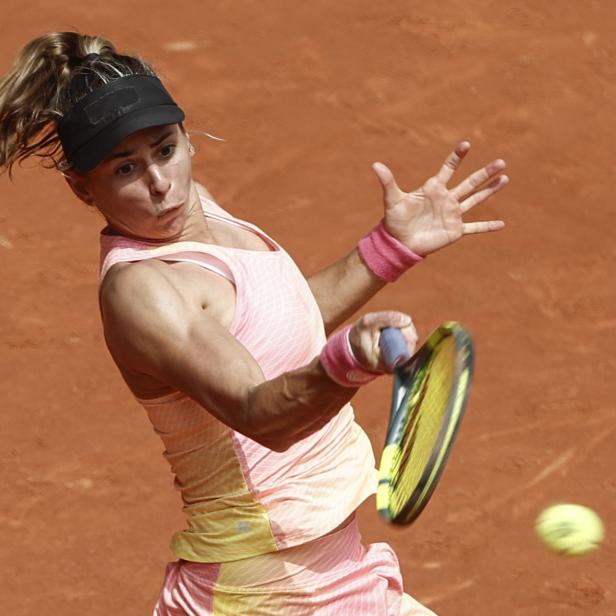 Eine Tennisspielerin mit Schirmmütze schlägt einen Ball auf einem Sandplatz.