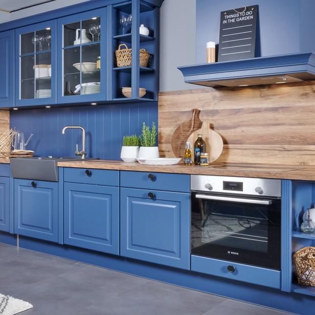 Moderne Küche mit blauen Schränken, Holzarbeitsplatte, Einbauofen, Spüle, Deko und Kräutertöpfen.