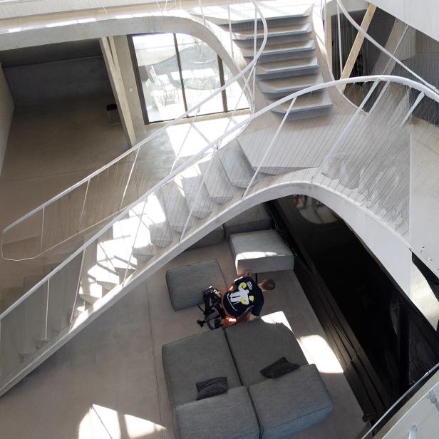 Moderne, helle Innenarchitektur mit geschwungener Treppe, grauen Sofas und einer Person, die auf dem Boden sitzt.