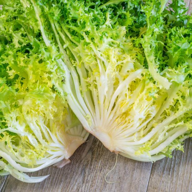 Aufgeschnittener Endiviensalat mit krausen, grünen und gelben Blättern auf einer Holzoberfläche.