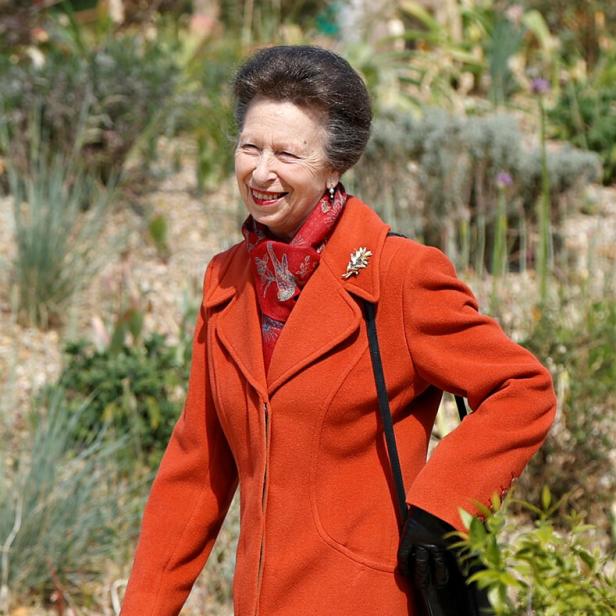 Eine lächelnde Prinzessin Anne trägt einen orangefarbenen Mantel und einen roten Schal im Freien.